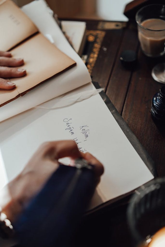 Crop author writing in notebook with feather at retro table